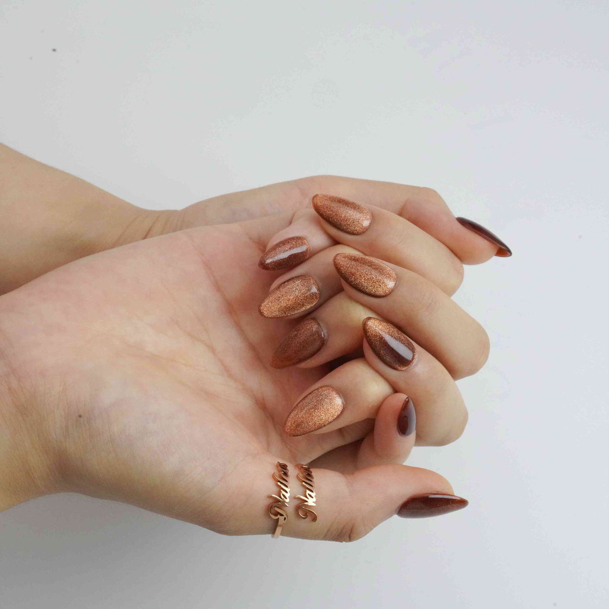 Close-up of Brown Cat Eyes almond-shaped press-on nails with copper shimmer and glossy brown highlights