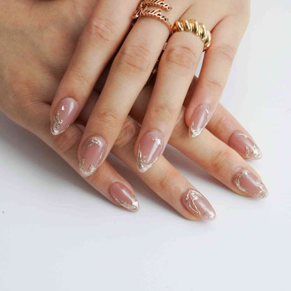 Mocha Swirl short almond press-on nails with a nude base and metallic accents, crossed-hand view