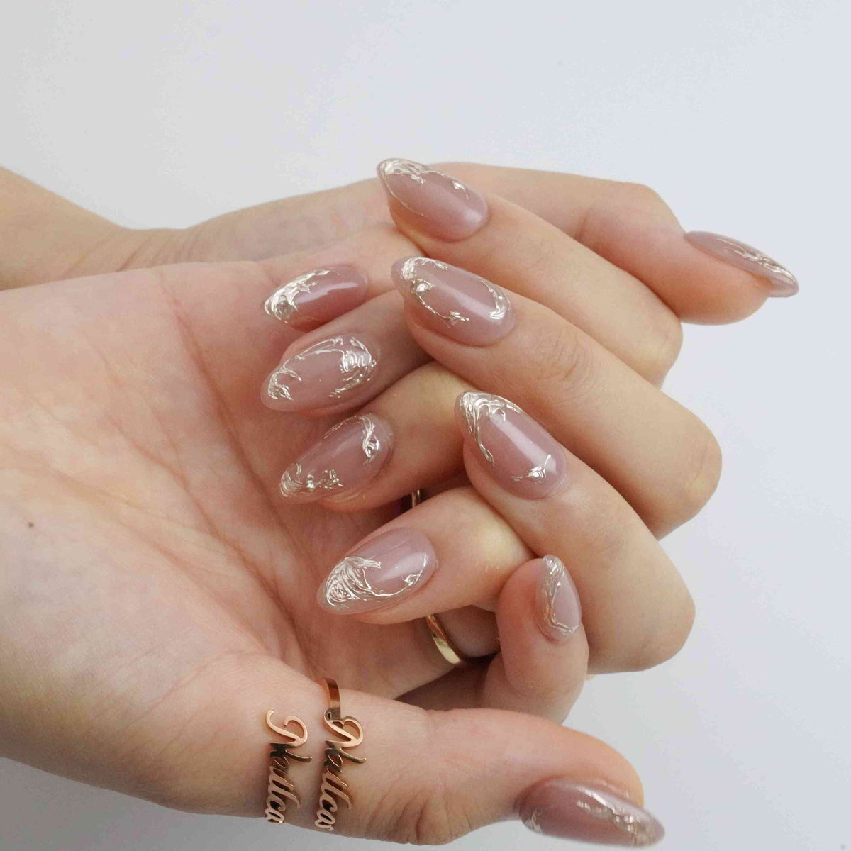 Close-up of Mocha Swirl nude short almond press-on nails showing raised metallic swirl details