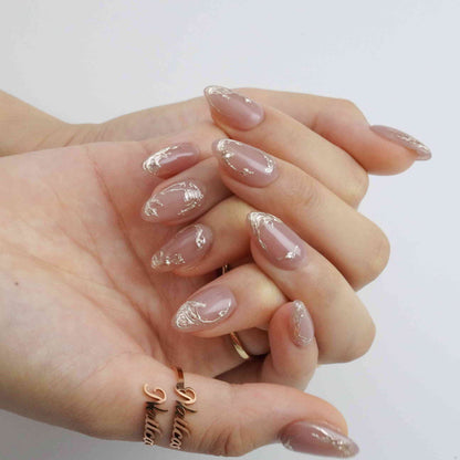 Close-up of Mocha Swirl nude short almond press-on nails showing raised metallic swirl details